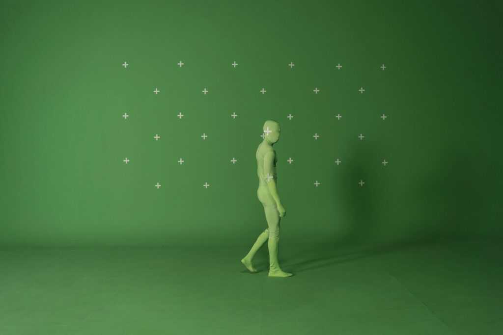 Person walking in a chroma key suit in a studio with green screen for video editing.