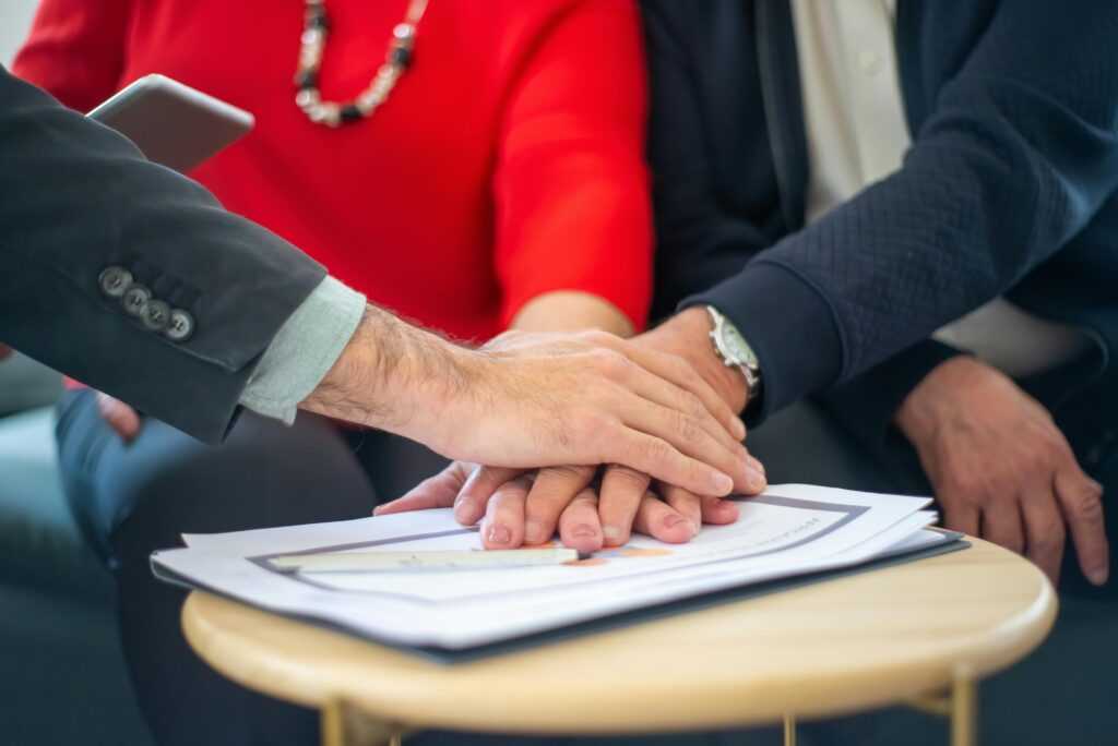 Business professionals collaborating, with hands united over important documents, symbolizing teamwork and unity.